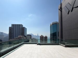 Rooftop terrace with glass railing overlooking a city skyline and harbor on a sunny day