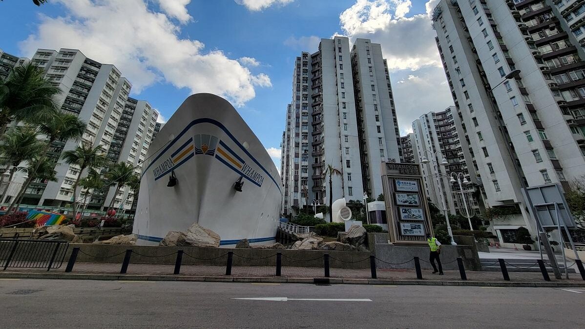 Large white ship sculpture with blueyellow accents in a city plaza backed by tall apartment buildings and palm trees on a sunny day