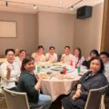 Group of friends and colleagues around a round dining table posing and giving thumbs up in a restaurant