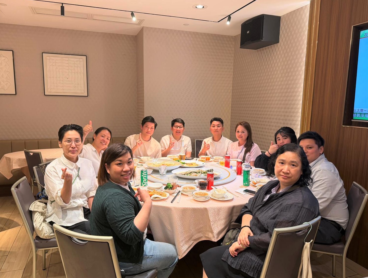 Group of friends and colleagues around a round dining table posing and giving thumbs up in a restaurant