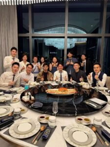 Group of colleagues in formal wear posing with thumbs up around a round dining table centered by a seafood platter