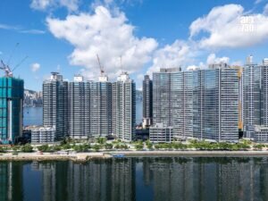 Row of glassy apartment towers along a riverfront with construction cranes and a blue sky behind them AM730 watermark in the top right corner