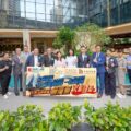 Group of professionals posing outdoors with a large promotional banner in front of a modern glass building