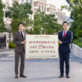 Two men in suits hold a large sign advertising a property development outdoors with the am730 logo visible