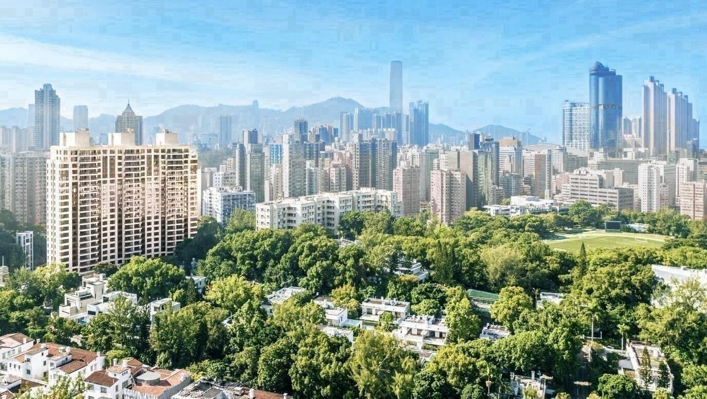 A city skyline with tall buildings rising behind a tree-filled park in the foreground.