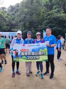 Four runners at the start line of a charity hike holding a colorful banner with 2026 against a forest backdrop