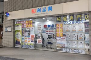 Storefront for a real estate agency with Chinese signage and large glass windows covered in property listings and colorful posters