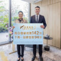 Two people in business attire pose indoors holding a large sign with Chinese text and the word MARINA
