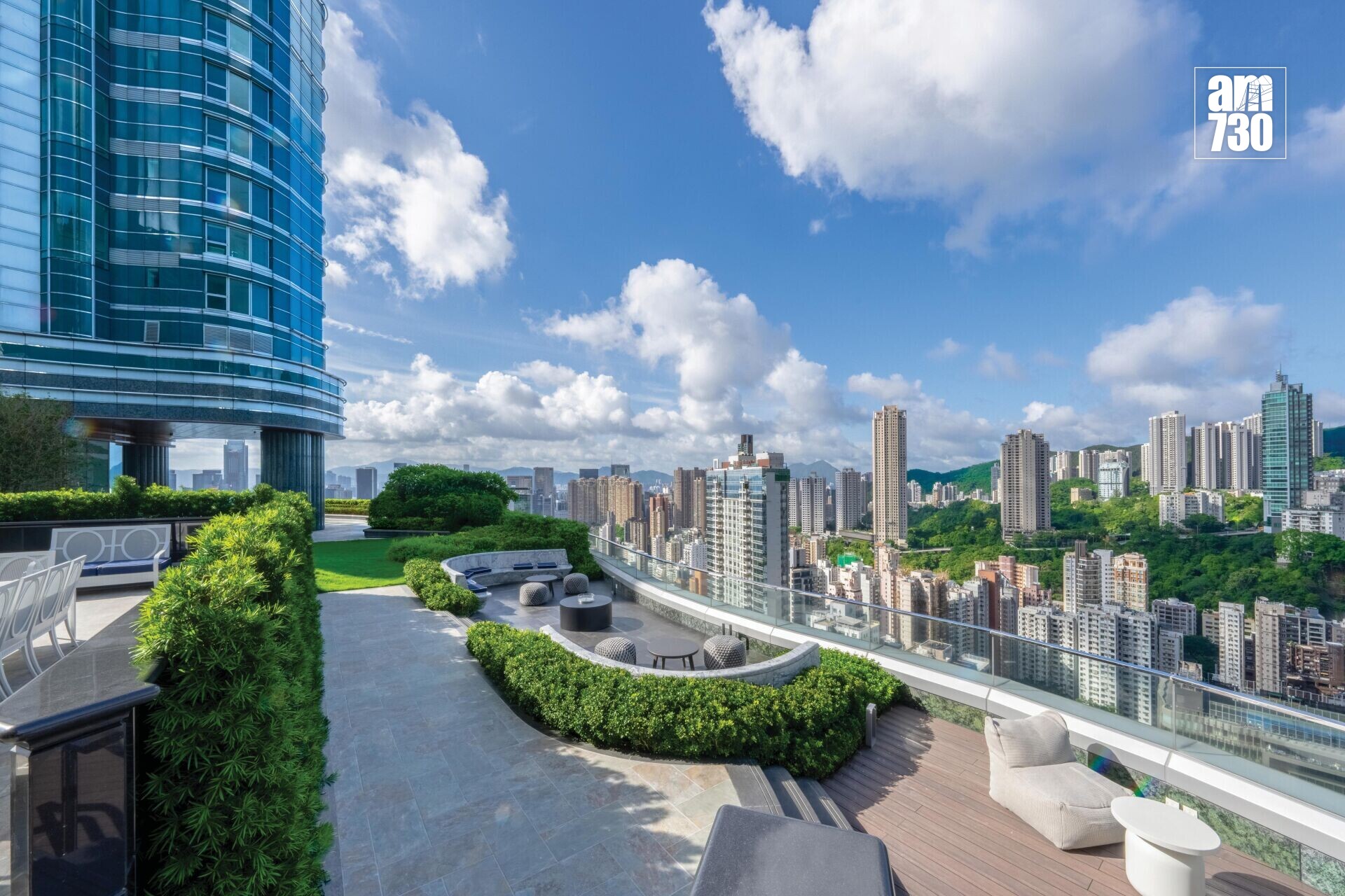 Rooftop terrace with outdoor seating, glass-front skyscraper on the left, and a city skyline under a blue sky.