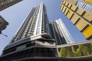 Low angle view of tall modern skyscrapers against a clear blue sky with a green wall feature at the base
