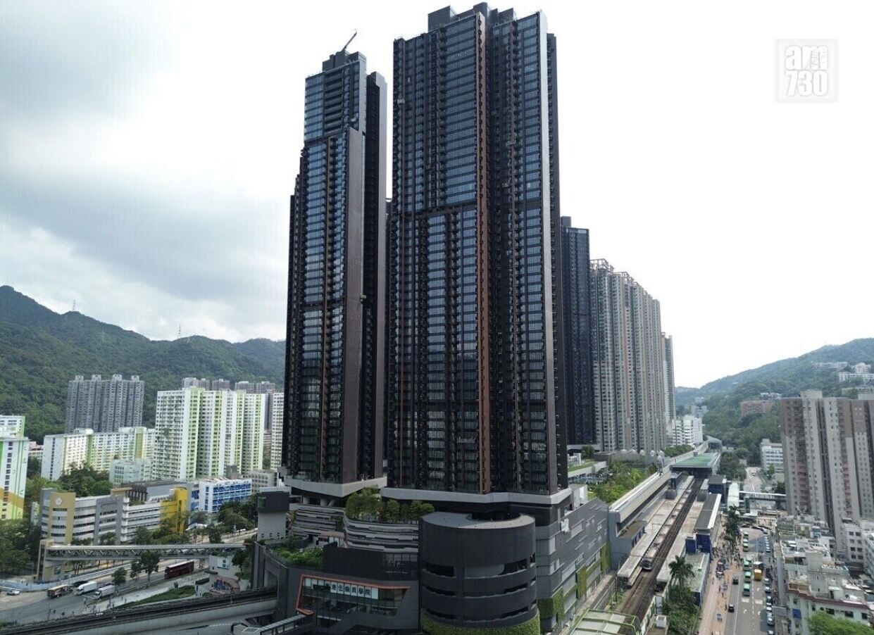 Tall modern residential skyscraper cluster rising above a city with hills in the background and a rail line nearby