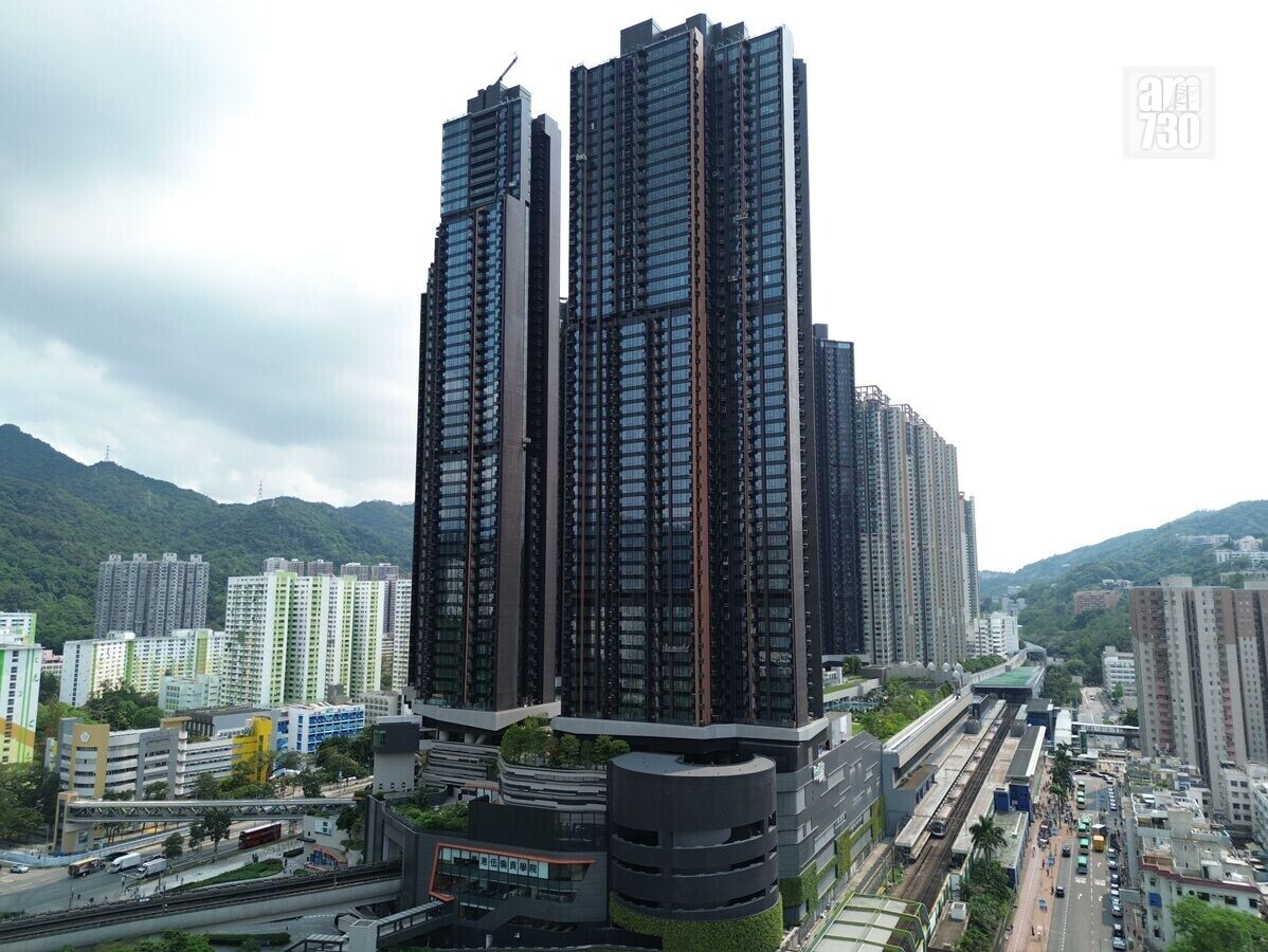Urban skyline with a cluster of tall glass towers, a rail line at street level, and green hills in the background