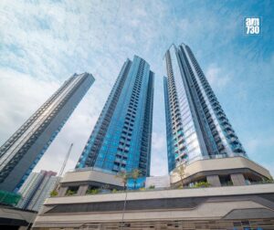 Three tall blue glass residential towers rise into a clear sky viewed from ground level