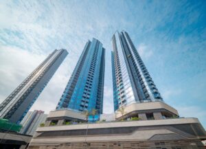 Three blue glass skyscrapers rise above a multi level podium against a clear blue sky with palms at the base