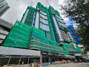 Under construction skyscraper wrapped in green safety netting with scaffolding and a street level construction barricade