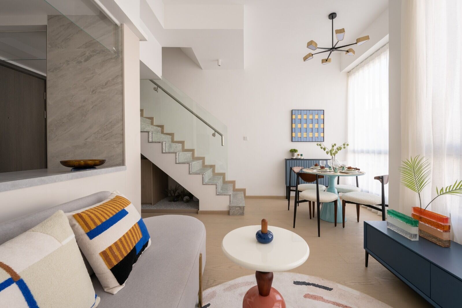 Bright, open living/dining area with a curved gray sofa, colorful striped cushions, and a white round coffee table in the foreground.