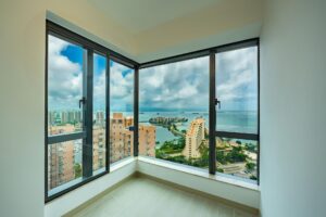 Corner room with floor to ceiling windows overlooking a coastal city and the sea beyond