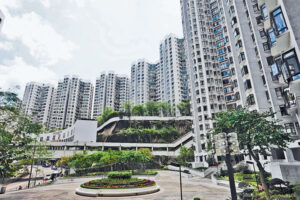 Tall white apartment buildings surround a landscaped courtyard with a circular flower bed and greenery near the center