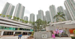 Cluster of tall residential towers surrounding a modern retail plaza with trees and a courtyard people walk nearby