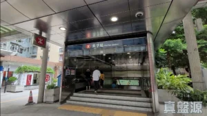 Mei Foo Station entrance with glass doors red MTR logo and people walking up the stairs under a metal canopy