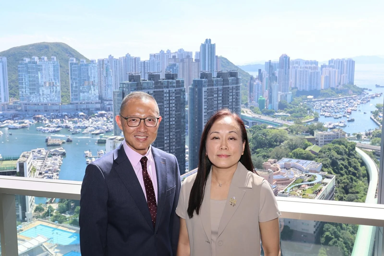 Two smiling professionals posing on a balcony with a city skyline and marina in the background