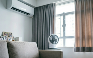 GeminiGeneratedImage49yfxz49yfxz49yf | 利嘉閣地產有限公司 Cozy living room corner with a beige sofa wall AC framed photos on a shelf a white fan by a window and magazines on a light wood coffee table