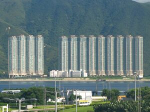 Row of tall blue gray apartment towers along a river with green hills in the background