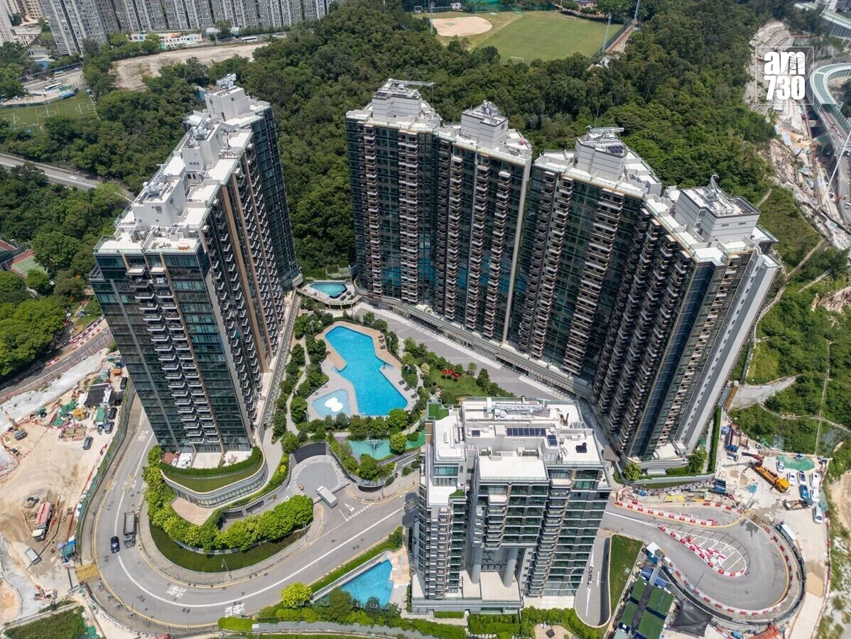 Aerial view of a modern U-shaped cluster of high-rise residential towers surrounding a central pool area and landscaped courtyards, with a curved road and construction nearby.