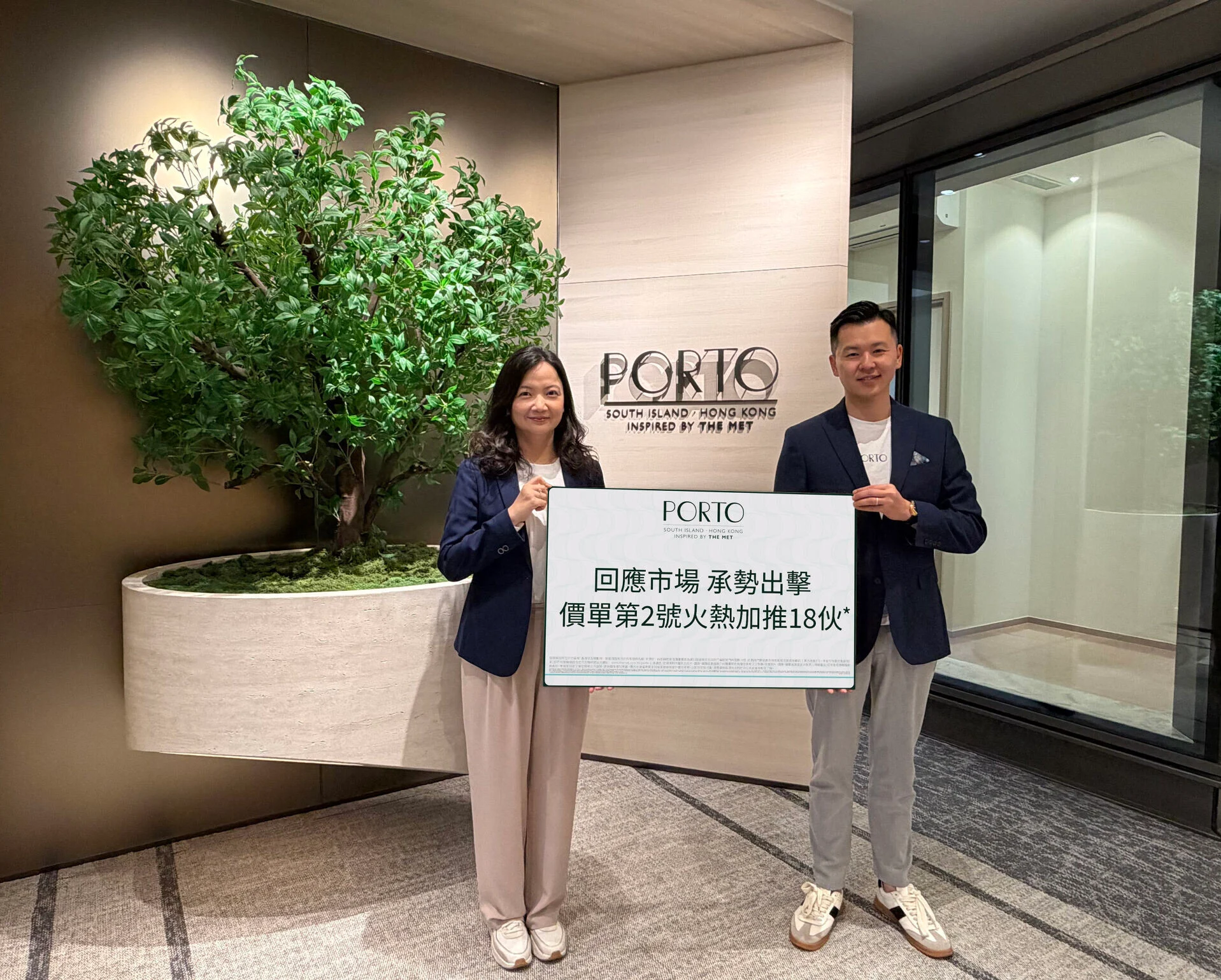 Two people in blazers stand in a modern lobby, holding a large sign with the PORTO logo and Chinese text.