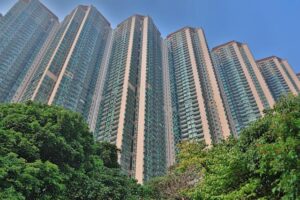 Cluster of tall glass high rise apartment towers rising above green trees under a blue sky