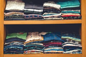 Stacks of folded shirts and fabrics arranged on wooden shelves in a wardrobe