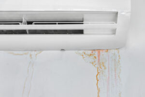 White wall mounted air conditioner with orange water stains dripping down the wall below it