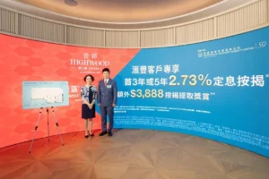 Two professionals pose in front of a redblue promotional backdrop for Highwood Phase 2 with an easel displaying a floor plan on the left