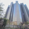 Tall modern glass skyscraper viewed from street level with trees in the foreground and AM730 logo in the top right corner