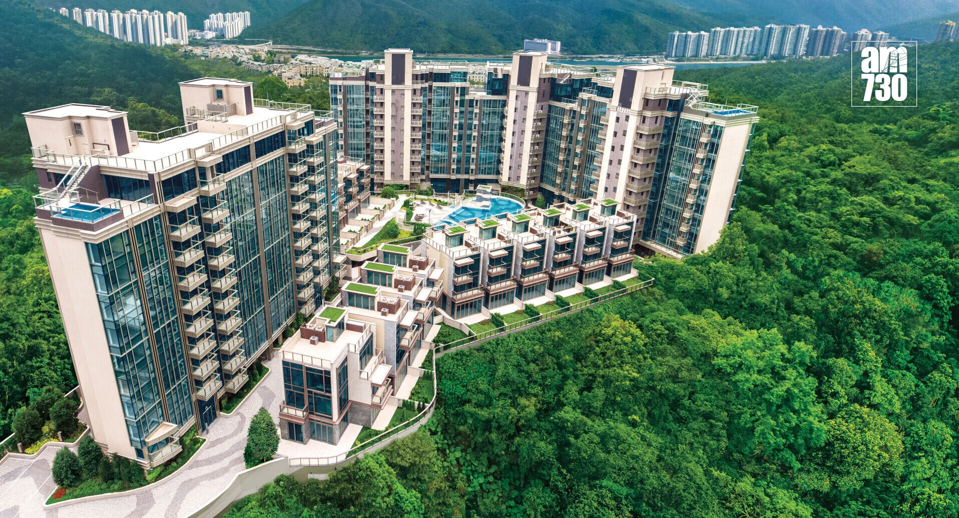Aerial view of a surrounding luxury apartment complex with glass facades, central pool, and green hills in the background, AM730 watermark in the top-right corner.