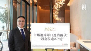 Asian man in a dark suit and blue tie smiling beside a large white poster on an easel in a modern well lit lobby with decorative lights in the background
