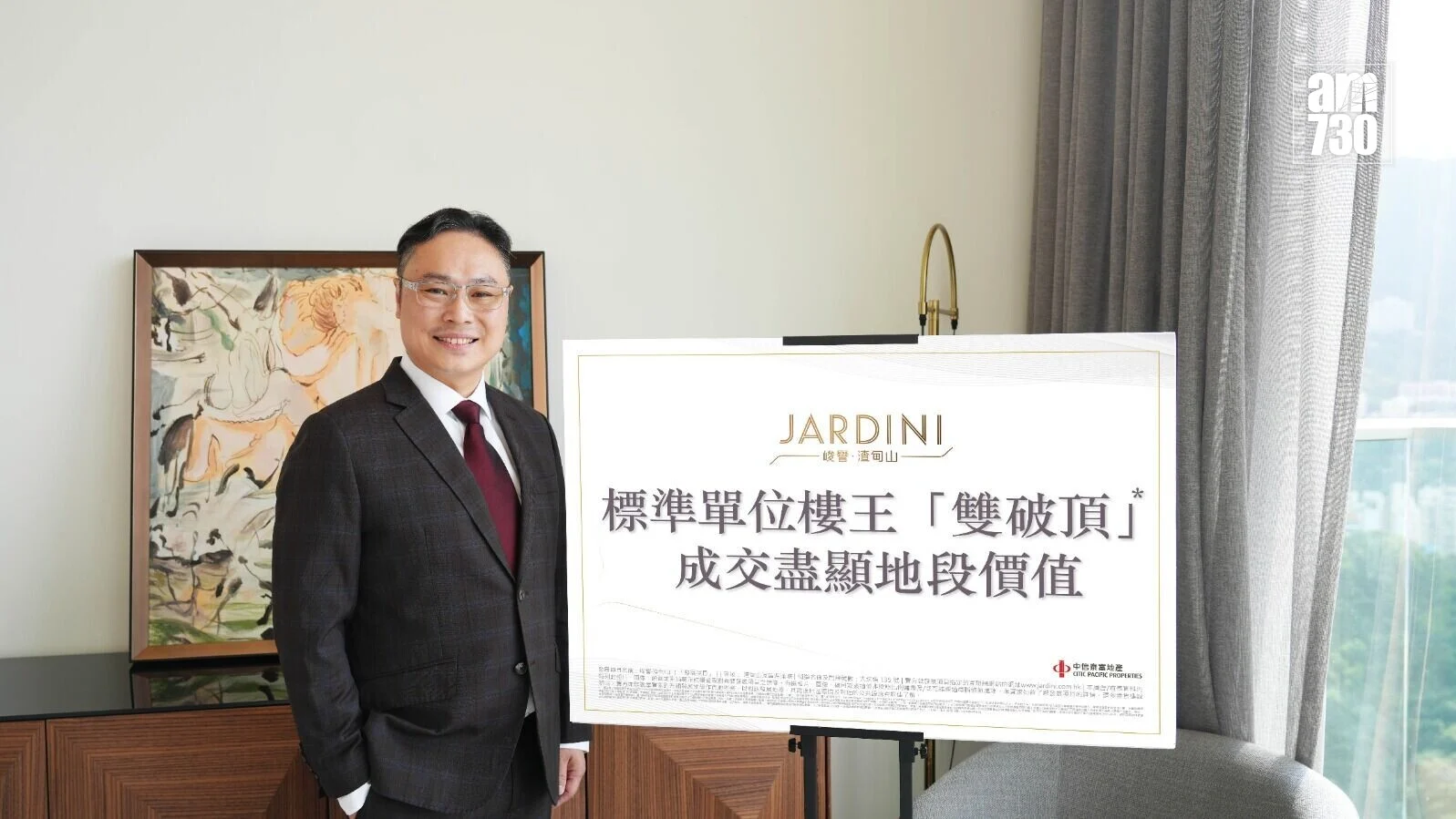 Man in a dark suit and red tie poses beside a large sign with Chinese text and the Jardini logo in a bright room.