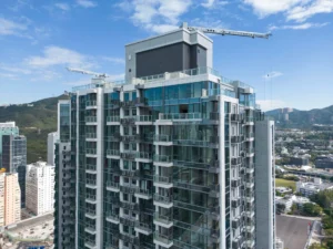 Modern glass apartment building under construction with cranes against a blue sky skyline in the background