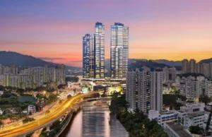 Twin skyscrapers illuminated at dusk rise above a busy city canal and curved highway with light trails