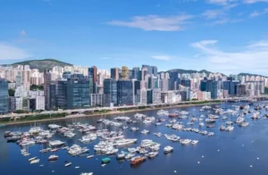 A coastal city skyline with tall modern buildings lined along a waterway filled with numerous moored yachts and boats
