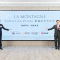 Three men in dark suits pose beside a large light blue banner reading LA MONTAGNE Collection Privée at a corporate event