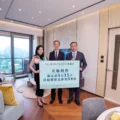 Three people in a modern living room hold a large blue poster with Chinese text