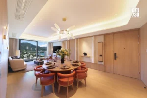 Luxurious dining area with a round table set for eight peach chairs and a floral centerpiece plus a large window showing mountains outside