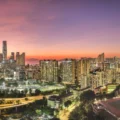Panoramic city skyline at sunset with an orange to purple sky dense high rise buildings and a foreground sports field