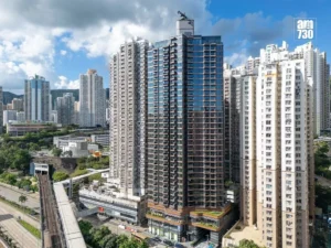Skyline of high rise residential towers under a blue sky with scattered clouds a prominent glass clad central building dominates the scene with an elevated rail track at street level on the left and a city logo in the top right corner