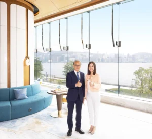 Two professionals in a bright glass walled lounge pose and give thumbs up with a city skyline and water in the background