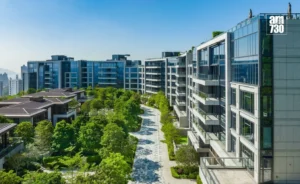 Modern residential complex with glass front buildings a tree lined pedestrian path and landscaped gardens along a central walkway A logo is visible in the top right corner