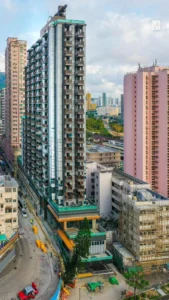 Tall modern high rise under construction in a dense city with a curved road and pink building to the right