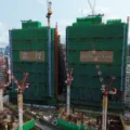 Two under construction high rise buildings covered in green netting with cranes nearby sign reads One Victoria Cove on the right tower