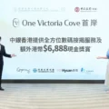Two presenters stand on a stage in front of a large screen reading 'One Victoria Cove' with Chinese text and sponsor logos visible.